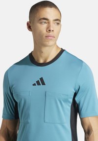 Maglietta sportiva blu con dettagli neri, maniche corte, due tasche frontali e un logo nero. Tessuto liscio, design aderente.