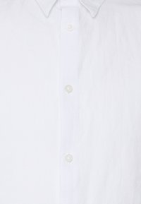 Camicia bianca in lino con colletto classico, chiusura a bottoni e una finitura testurizzata sottile per un tocco leggero e traspirante.
