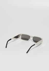 Sonnenbrille mit einem schlanken, rechteckigen silbernen Rahmen, grauen getönten Gläsern und schwarzen Bügeln; verfügt über Nasenpads und ein minimalistisches Design.