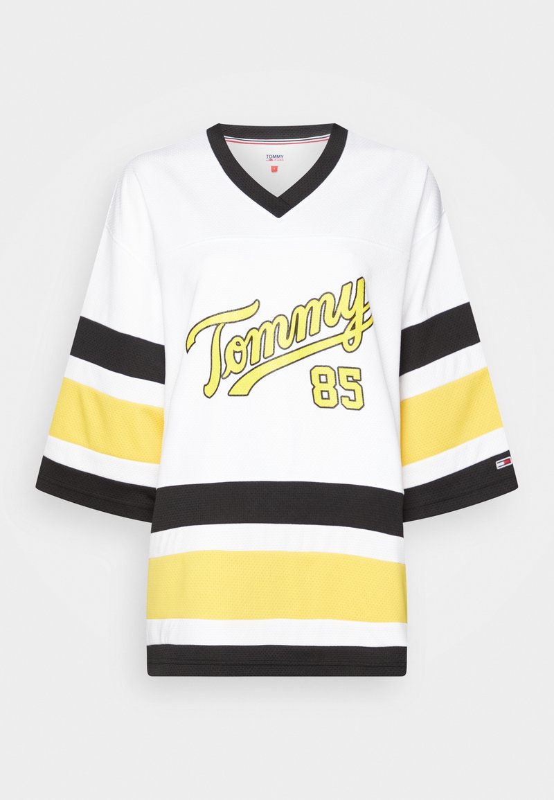 Bílý dres s žlutým nápisem "Tommy" a číslem "85". Rukávy a tělo zdobí černé a žluté pruhy. V-výstřih.