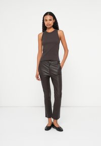 Top fără mâneci de culoare maronie, design ajustat; asociat cu pantaloni din piele maro închis, croi slim; pantofi plata negri completează ținuta. Fundal simplu.