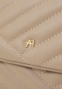 Borsa a tracolla trapuntata color caramello con cuciture diagonali, una texture liscia e un accento del logo dorato.