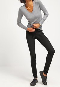 Camisa de manga larga gris con escote en V combinada con jeans ajustados negros y zapatillas negras. Textura suave, diseño ajustado y estilo minimalista.