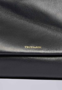Svart läderväska med en slät yta. Har en guld "TRUSSARDI"-logotyp som är tydligt synlig. Enkel, elegant design med rena linjer.