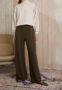 Ljus beige tröja med puffärmar och pärlaccenter, tillsammans med mörk olivgröna vida byxor. Mjuk textur och avslappnad passform.