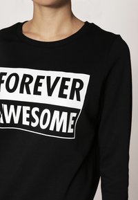 Černá mikina s kulatým výstřihem a dlouhými rukávy. Na přední straně se nachází výrazný bílý text "FOREVER AWESOME". Materiál: bavlna.