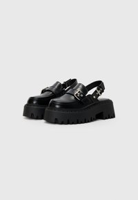 Black platform sandals with a smooth leather finish, buckle detail, and thick, jagged rubber soles. Open back design for easy wear.
