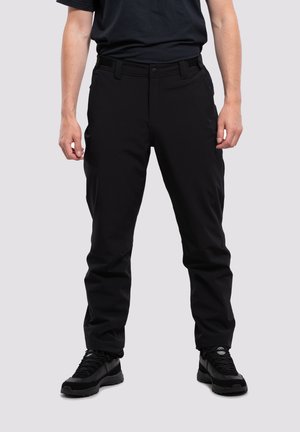 Pantalones negros de tela duradera con frente plano, trabillas para cinturón y bolsillos laterales; acompañados de calzado negro texturizado.