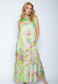 Bloomend maxi-jurk in lichtbeige stof met levendige groene accenten, met een losse pasvorm, mouwloos ontwerp en twee zakken aan de zijkant.