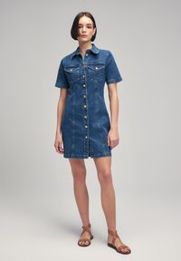 Robe chemise en denim, manches courtes, couleur bleu clair, fermeture à boutons sur le devant, deux poches poitrine, coupe slim, devant et dos plats, longueur au genou.