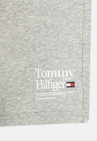 Šedá látka s bílým logem "Tommy Hilfiger", malou červenou, bílou a modrou vlajkou a názvy měst včetně New Yorku a Tokia vytištěné pod nimi.