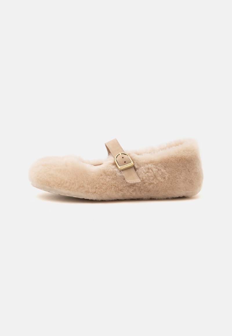Chausson Mary Jane beige et duveteux avec une seule bride en cuir et une boucle dorée, semelle plate, vue latérale sur fond blanc.