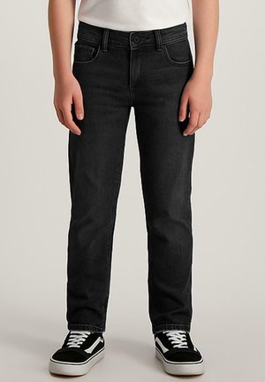 Jean noir en denim avec une coupe droite, un design à cinq poches et des surpiqûres contrastantes. Associés à des baskets noir et blanc.