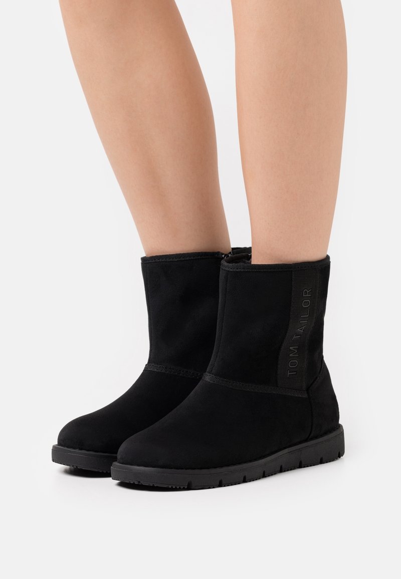 Bottines en suède noir avec un bout rond et une surface texturée. Présente un logo brodé "TOM TAILOR" sur le côté et une semelle en caoutchouc plate.