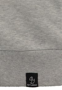 Tessuto grigio di felpa con orlo a costine. Presenta un piccolo logo quadrato nero con la scritta "KEYLARGO" nella parte inferiore. Texture morbida, design casual.