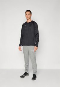 Čierne atletické tričko s dlhým rukávom a sivé nohavice. Hladká látka, priliehavý strih a logá na tričku aj nohaviciach. Čierne športové topánky.