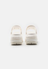 Zuecos blancos de Crocs con una superficie texturizada, correa en el talón y la marca "crocs". Presenta un acabado suave y suela de goma para mayor tracción.