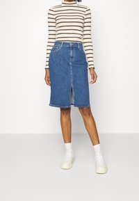 Jeans-Midirock mit einem Schlitz vorne, in hellblauer Waschung, fünf Taschen und Knopfverschluss. Kombiniert mit einem schwarz-weißen gestreiften Langarmoberteil.