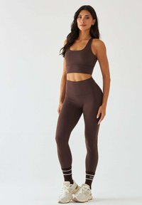 Brązowy zestaw sportowy składający się z krótkiego topu na ramiączkach i legginsów z wysokim stanem. Gładki, elastyczny materiał o dopasowanym kroju.