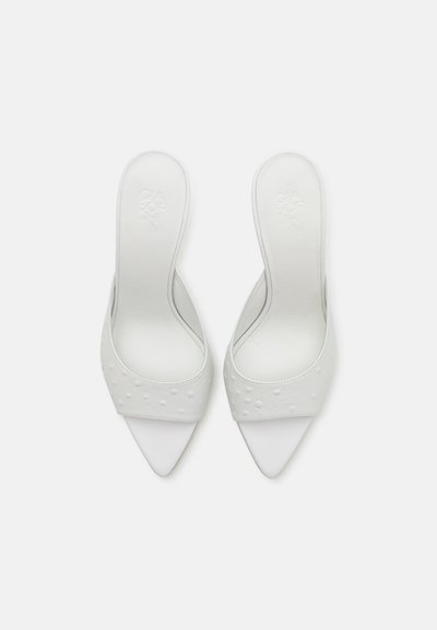Mules blancos de punta abierta con un acabado suave y patrones de puntos elevados en la parte superior. Presentan una punta afilada y un diseño de tacón bajo.