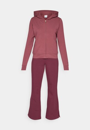 Bordeauxfarbener Hoodie mit Vorderreißverschluss und Taschen; kombiniert mit passenden weit geschnittenen Hosen. Beide bestehen aus weichem, dehnbarem Stoff mit einer glatten Oberfläche.