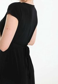 Svart klänning med korta ärmar, slätt tyg, figurnära bodice och ett knytband i midjan. Har en låg ryggdesign för extra stil.