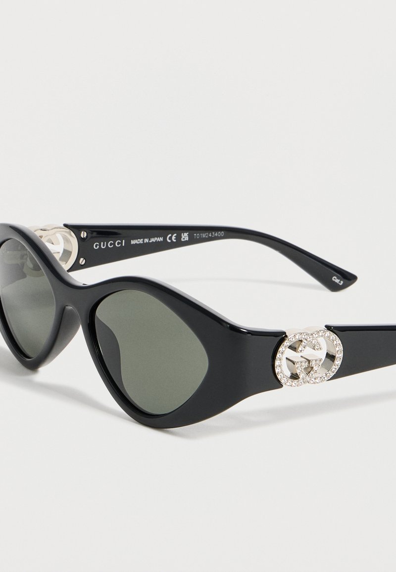 Schwarze ovale Sonnenbrille mit dunklen Gläsern und dem mit Strass besetzten Gucci Doppel-G-Logo am Bügel, hergestellt in Japan.