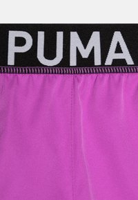 Czarna elastyczna talia PUMA z białym logo; żywotny fioletowy materiał o gładkiej fakturze; posiada marszczone przeszycia w pasie.