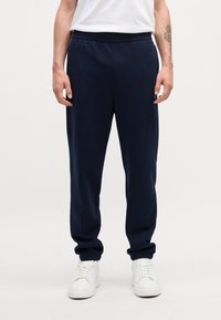 Pantalones de chándal azul marino hechos de una tela suave, con una cinturilla elástica y puños acanalados en los tobillos, combinados con zapatillas blancas.