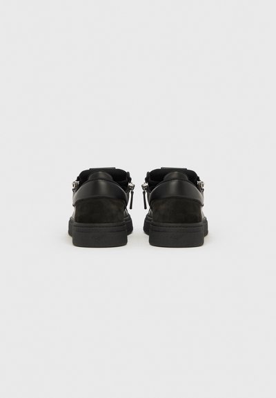 Pair of black low-top sneakers with leather and suede panels, featuring side zippers and embossed logos on the back soles.