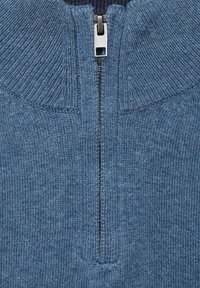 Närbild av en blå stickad tröja med delvis metalldragkedja och ribbat krage.