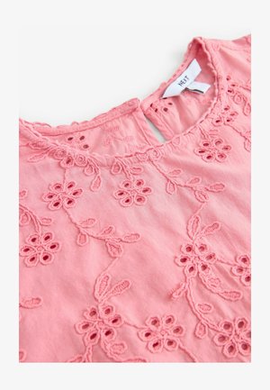 Roosa tikitud topp, millel on lillemustrid, võtmeaugu kaelus ja tekstuuriga õmblused kangapinnal.