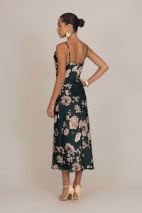 Robe florale verte avec des bretelles spaghetti ; présente de grandes fleurs de couleur claire, un corsage ajusté et une jupe fluide de longueur mi-longue en tissu satiné.