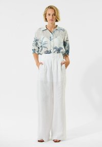Lichte, doorschijnende blouse met een blauwe botanische print, gecombineerd met luchtige, witte, high-waisted broeken. Beide items hebben een relaxte pasvorm.