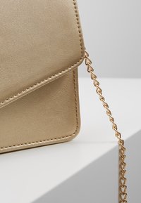 Guld faux läder axelväska med en texturerad yta, vikt flap och en metallkedja som accentuerar dess smala, rektangulära form.