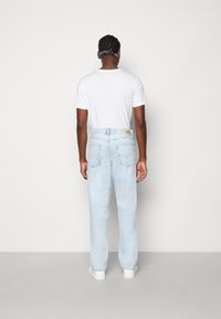 Ljusblå jeans med en avslappnad passform, med rak ben och bakfickor. Modellen har på sig en enkel vit t-shirt och vita sneakers.