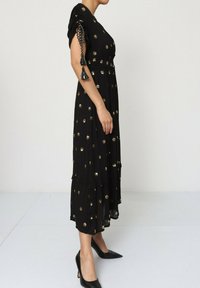 Robe noire avec un corsage ajusté et une jupe à volants, ornée d'embellissements circulaires dorés. Présente des manches courtes froncées et des accents à pompon.