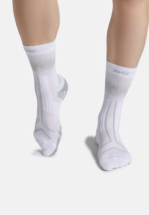 Persoon draagt witte sportsokken met grijze accenten, toont voor- en achteraanzicht van de voeten tegen een effen lichte achtergrond.
