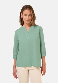 Blusa verde chiaro a tre quarti di manica con scollatura a V e tre bottoni decorativi sul colletto, realizzata in un tessuto morbido.