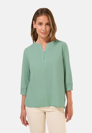 Blusa verde chiaro a tre quarti di manica con scollatura a V e tre bottoni decorativi sul colletto, realizzata in un tessuto morbido.
