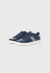 Marineblaue Sneaker mit niedrigem Schnitt und weißen Sohlen, Schnürung vorne und seitlichen Streifen mit Markentext auf einem schlichten hellen Hintergrund.