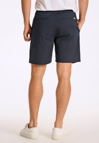 Mörkblå shorts i lätt tyg, med resårmidja och två bakfickor, bärs med vita sneakers.