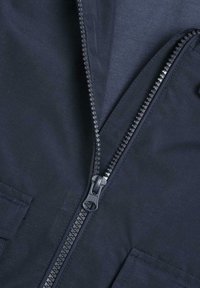 Veste bleu marine avec une fermeture éclair robuste, une texture de tissu lisse et des poches avec des coutures renforcées pour la durabilité et la fonctionnalité.