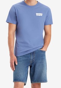 Camiseta de algodón azul claro con mangas cortas y un logo blanco de Levi's en el pecho, combinada con pantalones cortos de mezclilla azul.