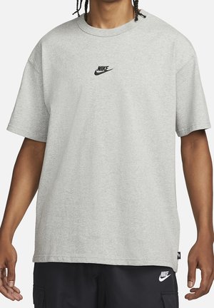 Osoba nosząca jasnoszarą koszulkę Nike z małym czarnym logo Nike na klatce piersiowej oraz czarne szorty Nike z białym logo na udzie.