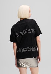 Crna oversized majica s kratak rukavima koja na leđima sadrži odvažne bijele natpise "LAGERFELD". Izrađena od pamuka, sa slobodnim krojem.