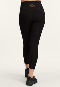 Zwarte leggings met een hoge tailleband met een oranje lotuslogo. Het materiaal is glad met een slim-fit ontwerp, dat net boven de enkel eindigt.