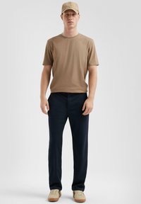 Tan korte mouwen t-shirt, marineblauwe broek en beige pet. Schoenen zijn crème met zwarte accenten. Eenvoudig, slim design en een soepele textuur.