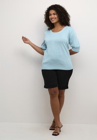 Top azzurro chiaro a maglia con maniche a sbuffo, abbinato a pantaloni corti neri con orlo arrotolato e sandali neri con cinturini. Tessuto liscio, vestibilità rilassata.