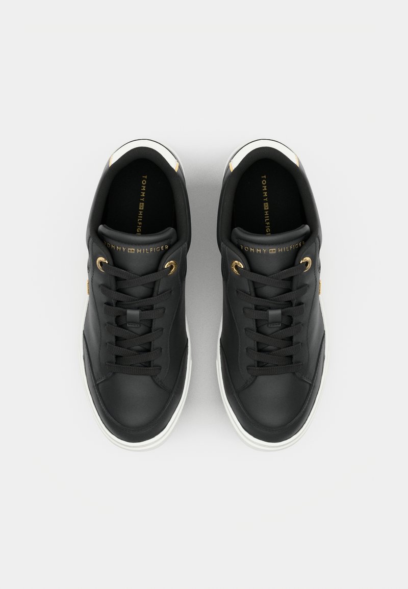 Sneaker in pelle nera con suole in gomma bianche, dotate di occhielli dorati, lacci neri e un logo dorato sulla linguetta.